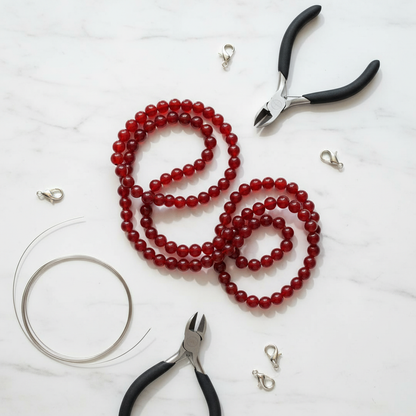 Red carnelian 6mm bead strands on white marble with jewellery-making tools