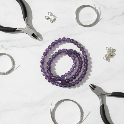 Purple amethyst 6mm bead strands on white marble with jewellery-making tools