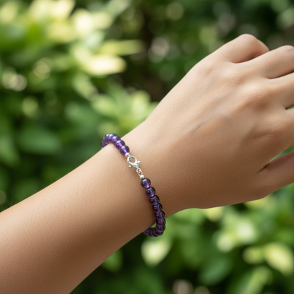 Model with olive skin tone wearing purple amethyst 6mm bead bracelet, outdoor green foliage background